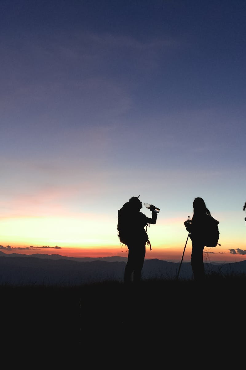 Group of hikers silhouetted against a vibrant sunset, enjoying an adventurous outdoor trek.